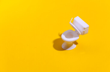 Mini white toilet on yellow background with deep shadow. Minimalism.