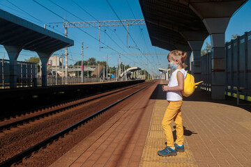 Little girl in a T-shirt and jeans and a medical mask waiting for the train