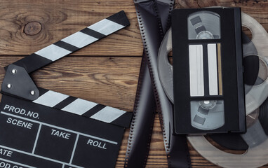 Movie clapper board, film reel, tape and video cassette on wooden background. Cinema industry,...
