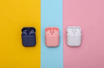 Different colors Wireless headphones with charging case on colorful pastel background. Top view