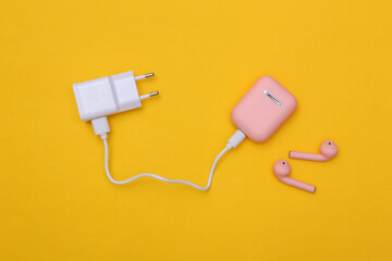 Wireless headphones with charging case and charging adapter on yellow background. Top view