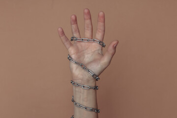 The hand wrapped in a metal chain on a brown background. Suppression of freedom or imprisonment, hostage