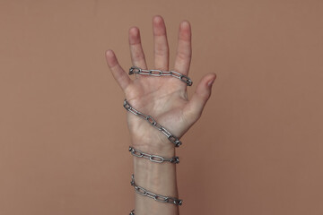The hand wrapped in a metal chain on a brown background. Suppression of freedom or imprisonment,...