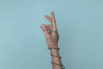 The hand wrapped in a metal chain on a blue background. Suppression of freedom or imprisonment,...