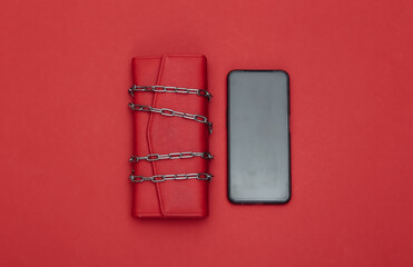 Leather wallet wrapped in a steel chain and smartphone on red background.