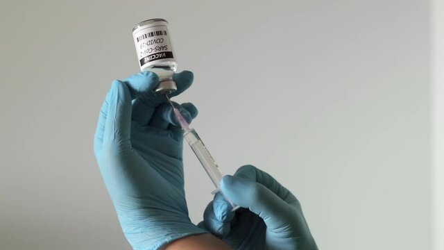 Close up shot of nurse's hands wearing surgical gloves,  holding syringe sucking out vaccine for covid-19.
