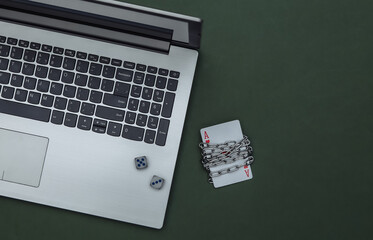 Laptop with ace of hearts wrapped in a steel chain and dice on a green background. Online casino ban