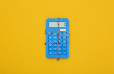 Blue calculator wrapped in steel chain on a yellow background. Top view