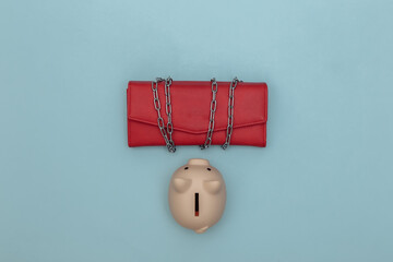 Leather wallet wrapped in a steel chain and piggy bank on blue background. Top view