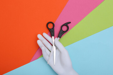 Mannequin hand holding hair scissors on colorful background. Minimalism beauty concept. Top  view