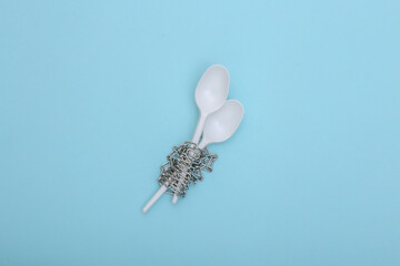 Plastic spoons wrapped in a steel chain on blue background. Diet concept