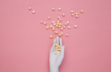 A lot of mini marshmallows in a white mannequin hand on pink background. Top view