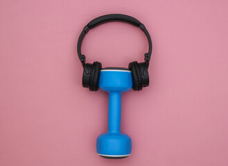 Dumbbell with stereo headphones on pink background. Sport concept. Top view