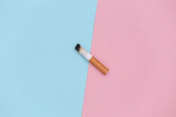 Smoked cigarette on a blue-pink pastel background. Bad habit. Top view
