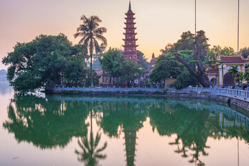 Obraz premium Hanoi buddhist pagoda (Tran Quoc Pagoda) on West Lake at Hanoi, colorful sunset, illuminated temple, water reflection. Vietnam travel.