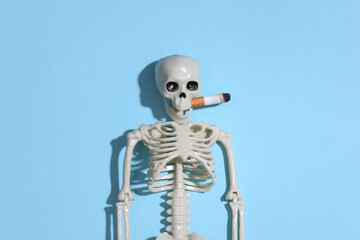 Smoking skeleton with a cigarette in the mouth against a bright blue background. Smoking kills