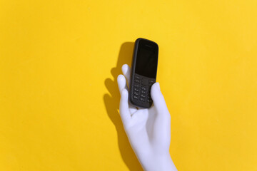 Mannequin's hand holds a push-button telephone on a yellow background. Top view