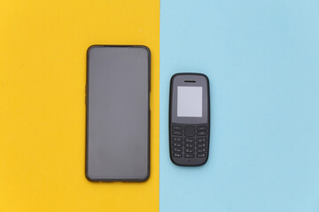 Push-button telephone and modern smartphone on a blue-yellow pastel background. Top view