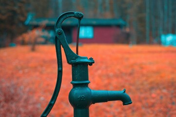 A old nostalgic hand water pump made of cast iron near a cottage in the woods.