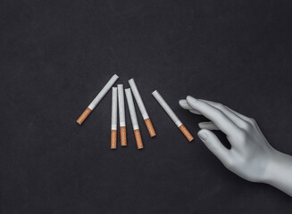Mannequin's hand touches cigarettes on a black background. Smoking addiction