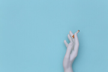 Mannequin hand holding cigarette on blue background