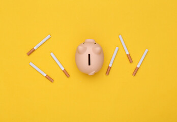 Piggy bank with cigarettes on yellow background. Top view