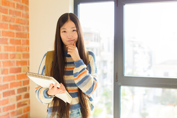young asian woman looking serious, confused, uncertain and thoughtful, doubting among options or...