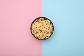 Bowl of corn rings on blue-pink pastel background. Snacks. Top view