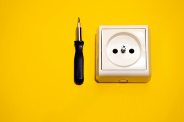 screwdriver and disassembled socket on a yellow background. Electrical work concept.