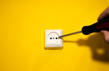 White electrical plug with screwdriver on yellow background. European white outlet in the center in yellow background . Space for your text.