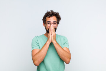 young bearded man looking happy, cheerful, lucky and surprised covering mouth with both hands