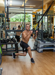 Fototapeta na wymiar Muscular naked torso man training with fitness trx system in the gym. Bodybuilder exercising his muscles with suspension straps