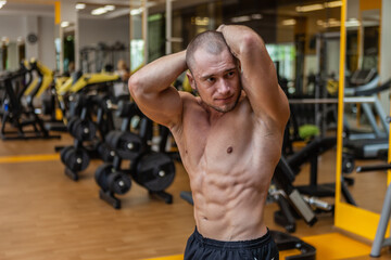 Muscular male bodybuilder with naked torso posing in the gym