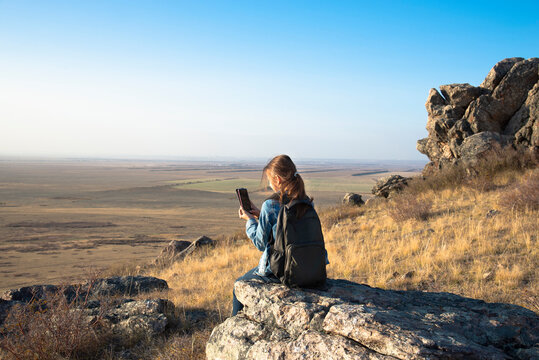 A girl with a backpack sits on a rock above the valley in the Golden hour and takes photos. Concept local hiking
