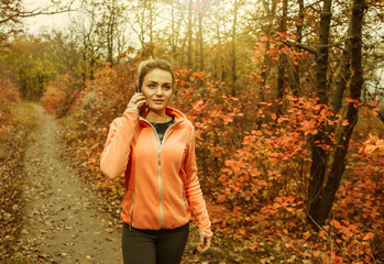 Young attractive woman in sportswear talking on the phone while walking along a path with red autumn leaves in the forest