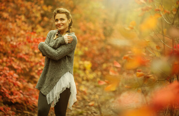 Young cheerful frozen woman in the autumn forest with reddened leaves. Art portrait