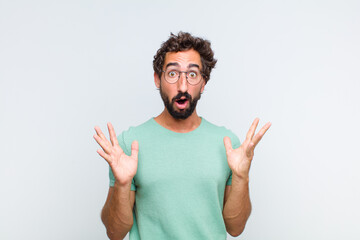 young bearded man looking shocked and astonished, with jaw dropped in surprise when realizing...