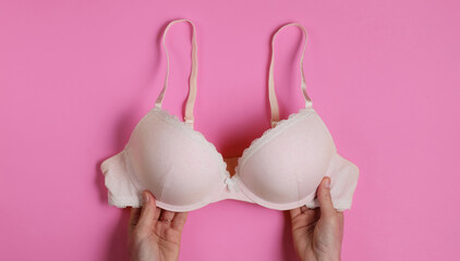 Female hands hold bras on pink studio background. Top view - obrazy, fototapety, plakaty