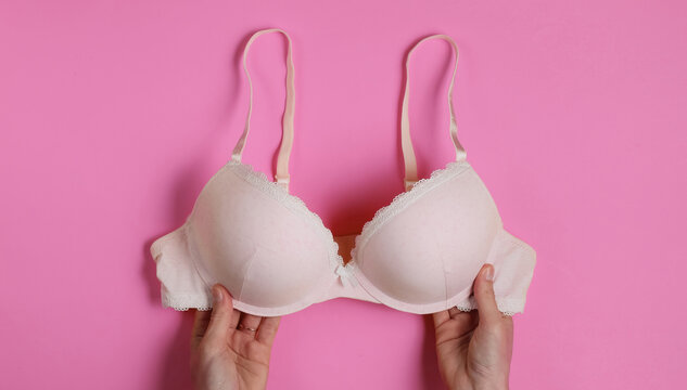 Female Hands Hold Bras On Pink Studio Background. Top View