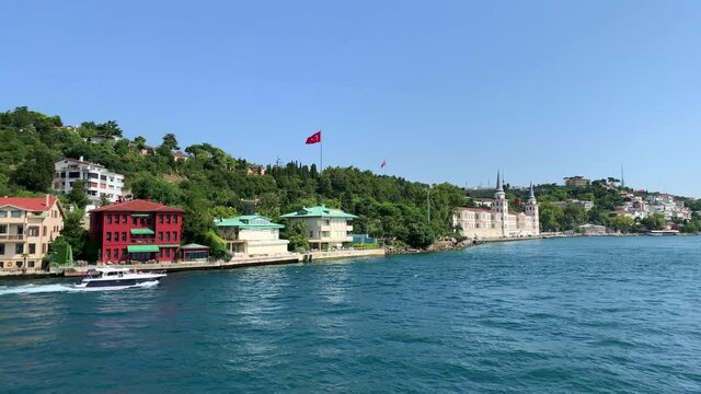 Footage of yacht passing in Kandilli / Cengelkoy area of Istanbul on Bosphorus strait. Kuleli military school is in the view. Beautiful scene. It is a sunny summer day. Camera moves forward.