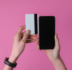 Hand with smart bracelet holding bank card and smartphone on pink background. Cashless payment, online shopping. Top view.