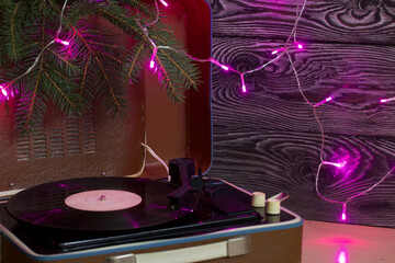 Old turntable. Nearby there are spruce branches and burning festive garlands. Against the background of pine boards.