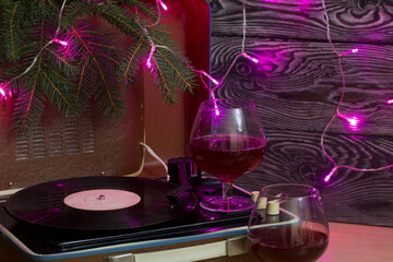 Old turntable. There are glasses of wine nearby. Spruce branches and burning festive garlands. Against the background of pine boards.