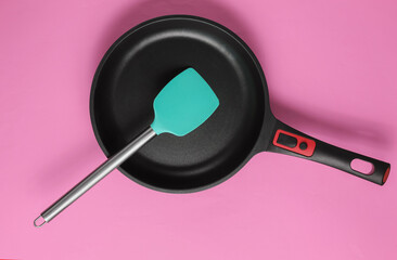 Non-stick pan with cooking spatula on pink background. Cooking minimalism concept. Studio shot. Top view