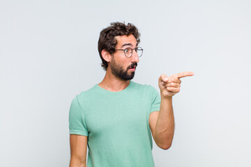 young bearded man feeling shocked and surprised, pointing and looking upwards in awe with amazed,...