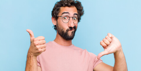 young bearded man feeling confused, clueless and unsure, weighting the good and bad in different...