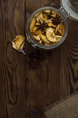 Homemade crispy sun dried organic apple slices. Close up of apple chips with spice in glass jar on brown wooden background with copy space for text
