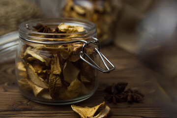 Homemade crispy sun dried organic apple slices. Close up of apple chips with spice in glass jar on brown wooden background with copy space for text

