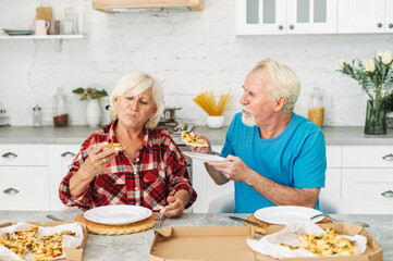 Senior couple eating pizza in the kitchen