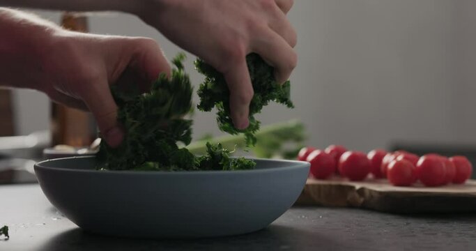 Slow motion man hands put kale leaves in blue bowl on concrete surface